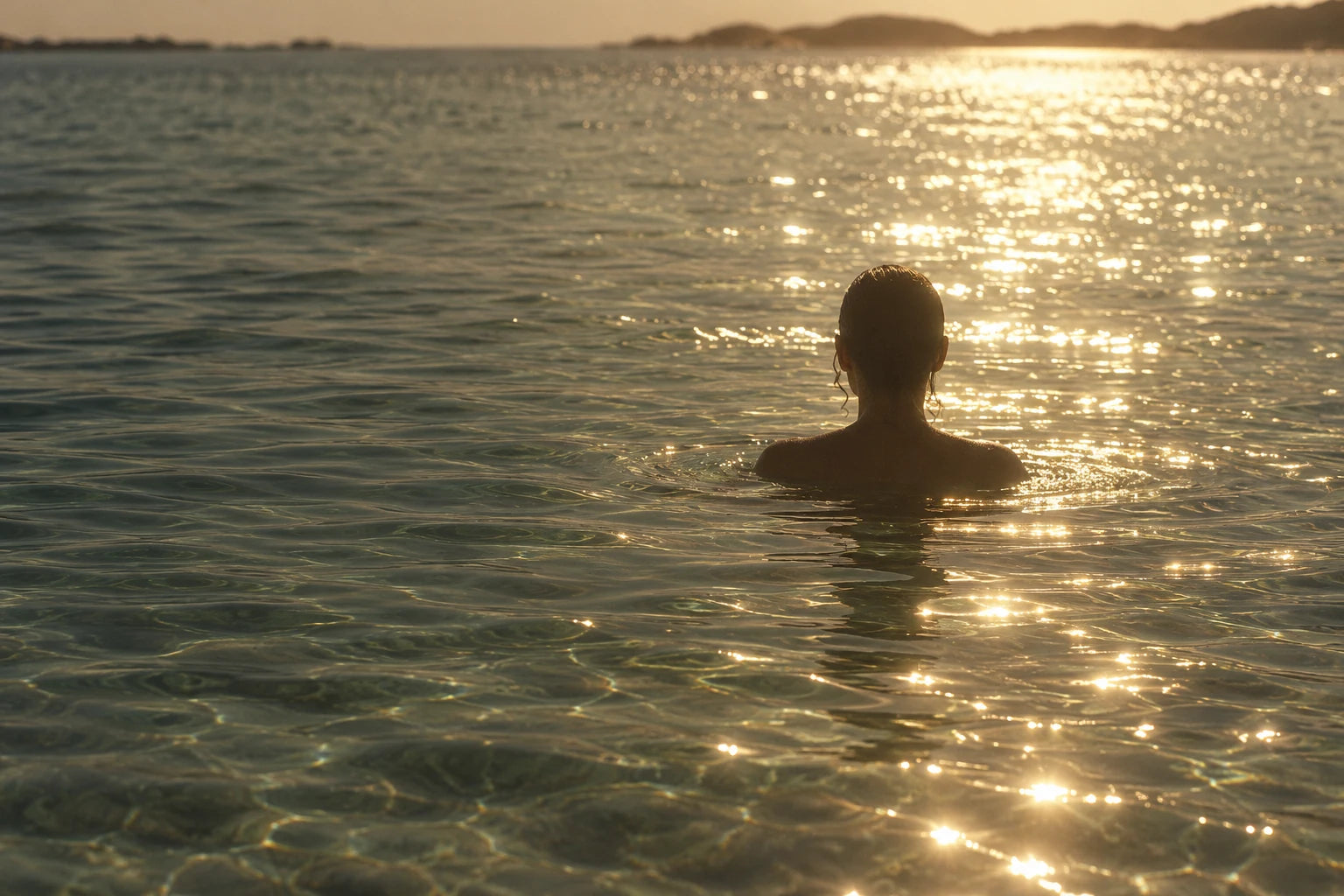 A person seen from behind in clear shallow water, with golden sunlight scattered across the ripples.